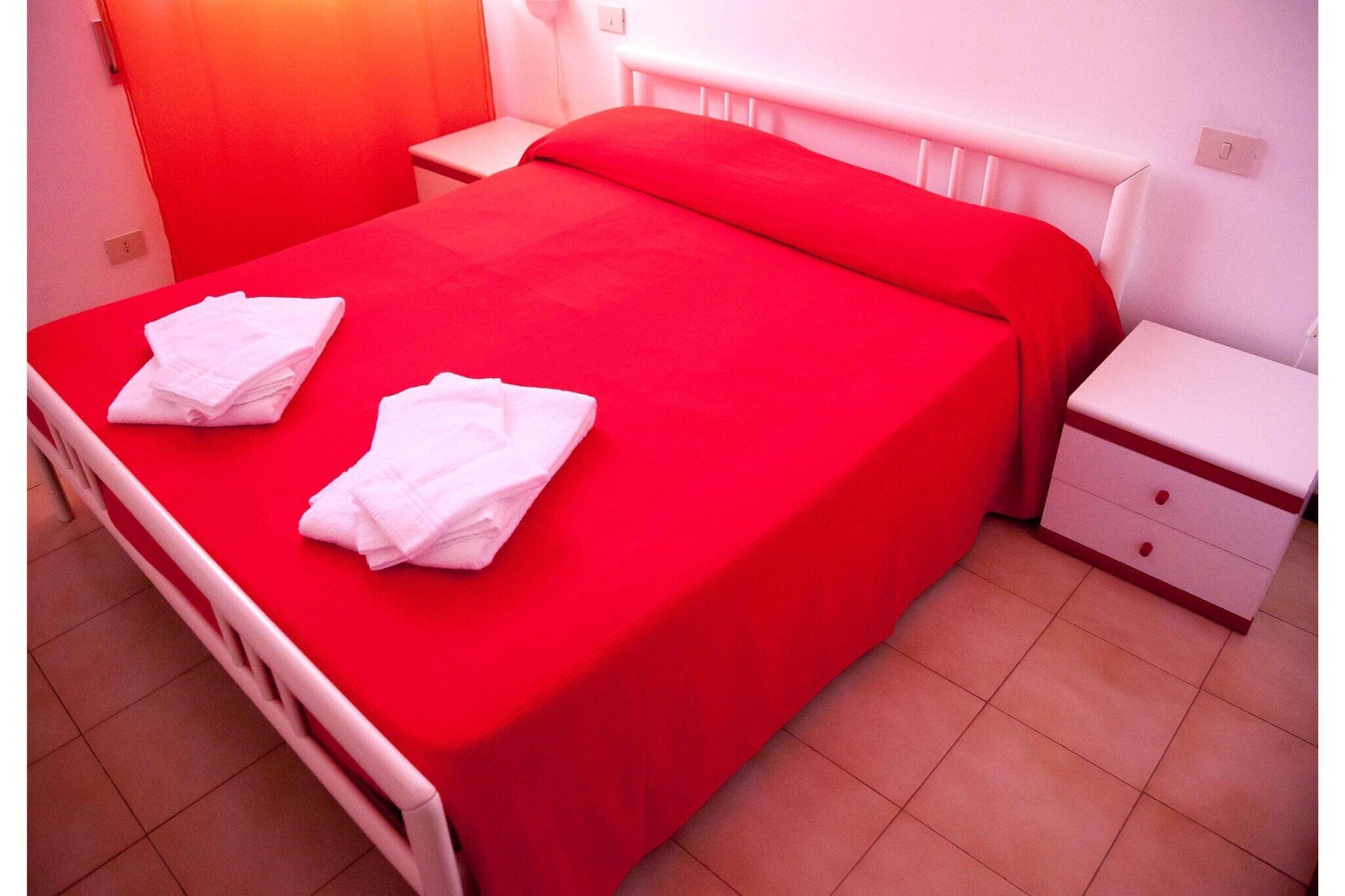 Ein ordentlich bezogenes Bett mit roter Bettwäsche und zwei gefalteten weißen Handtüchern auf der linken Seite.