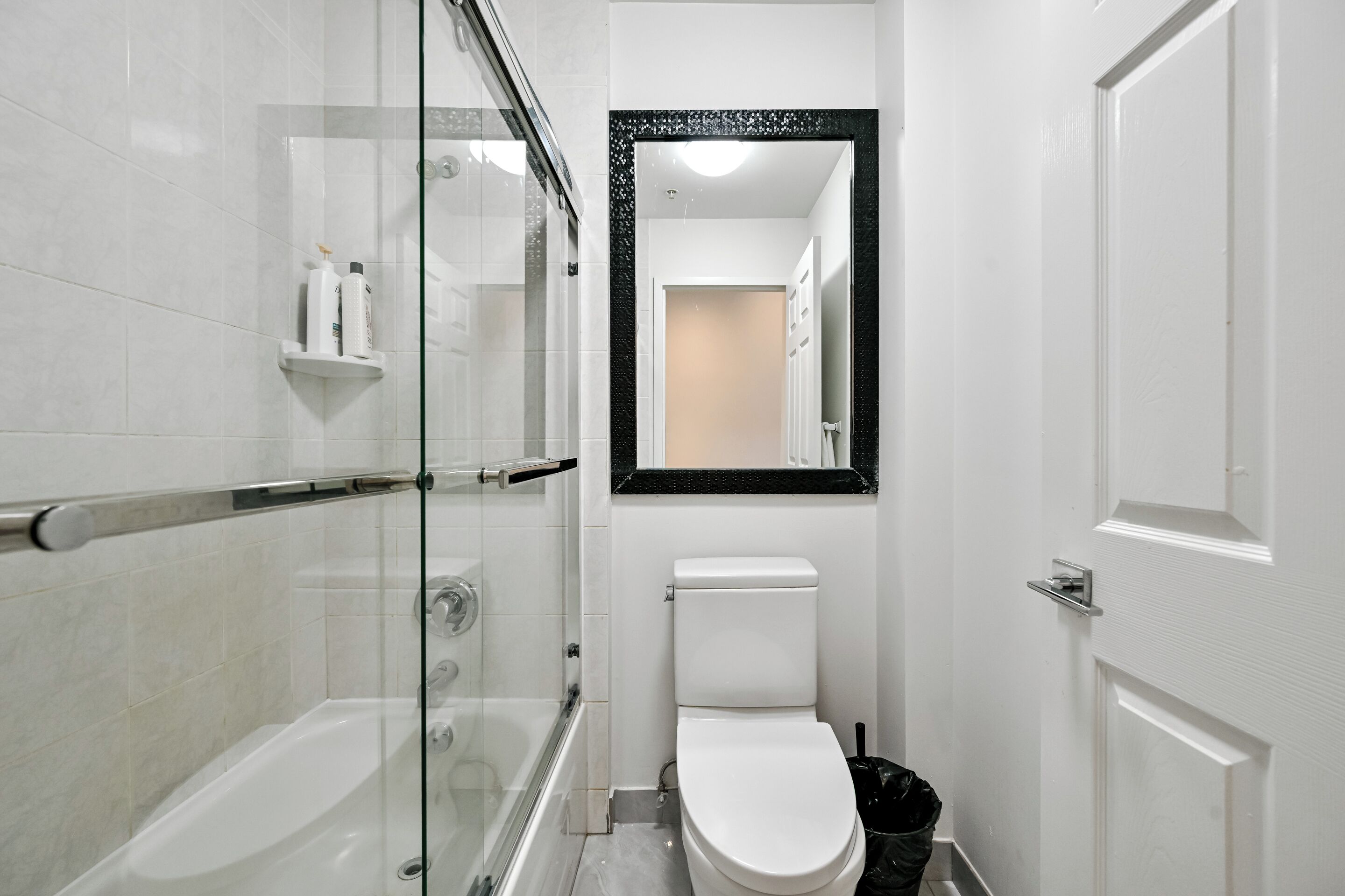 A bathroom with a glass-enclosed shower, a white toilet, and a black trash bin.