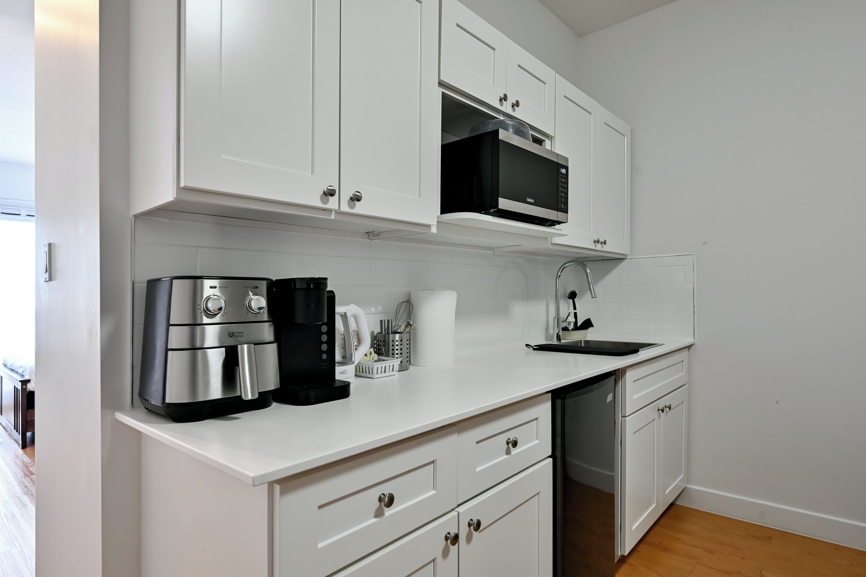 A modern kitchen with white cabinets, a built-in microwave, a coffee maker, and a dishwasher.