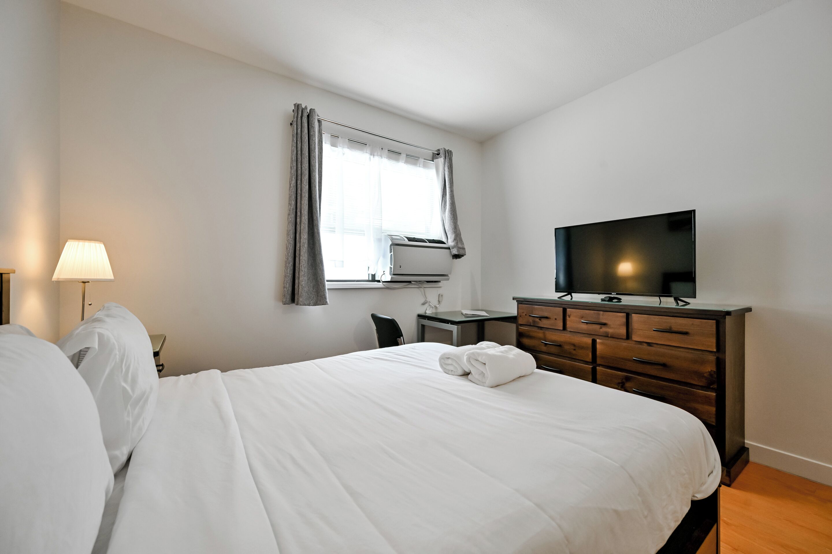 Una habitación de hotel con cama, escritorio, televisor y ventana con cortinas.