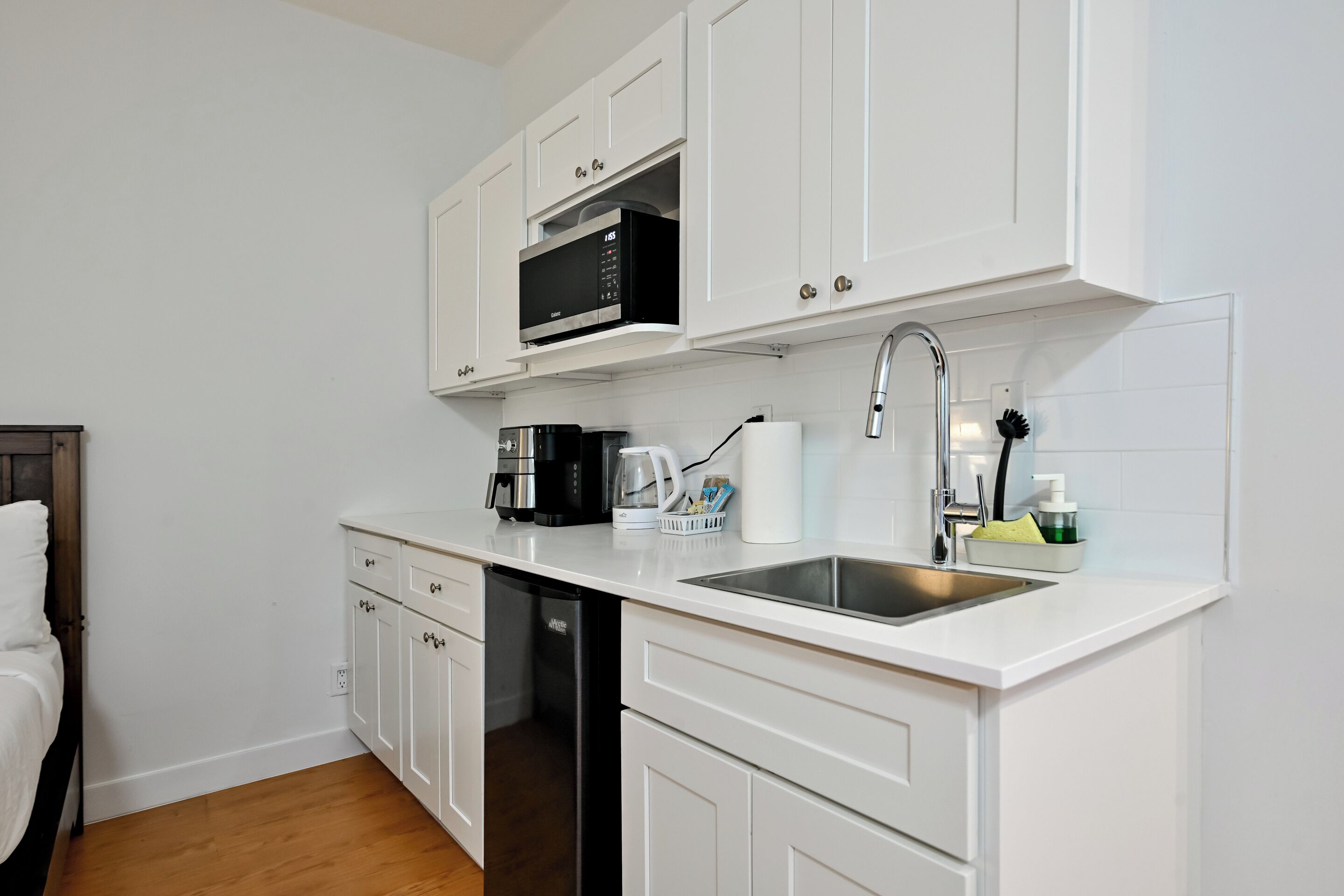 Una cocina compacta con armarios blancos, microondas integrado, cafetera y lavabo.