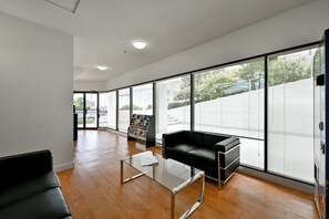 A spacious room with a black leather sofa, a glass coffee table, and large windows with blinds. - NEW ROYAL INN (New Westminster)