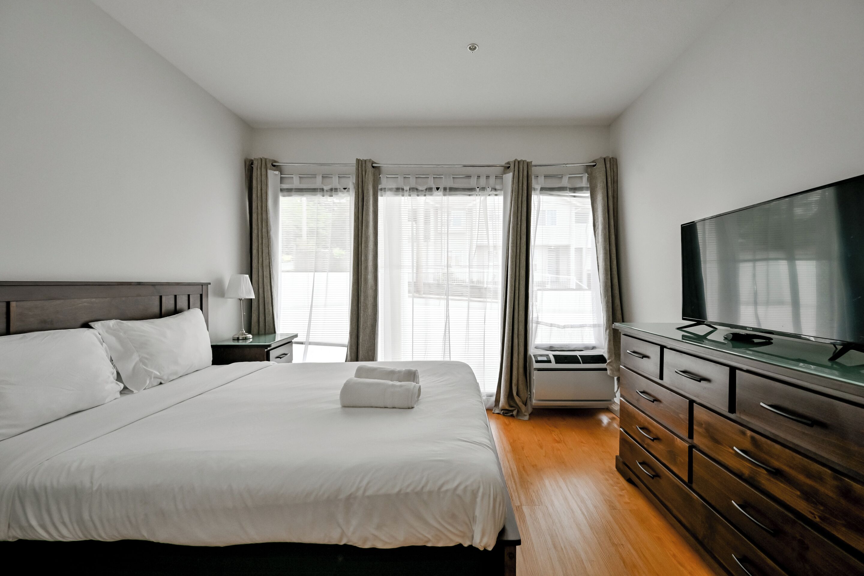 Ein Hotelzimmer mit einem Bett, einem Fernseher, einer Kommode und einem Fenster mit Vorhängen.