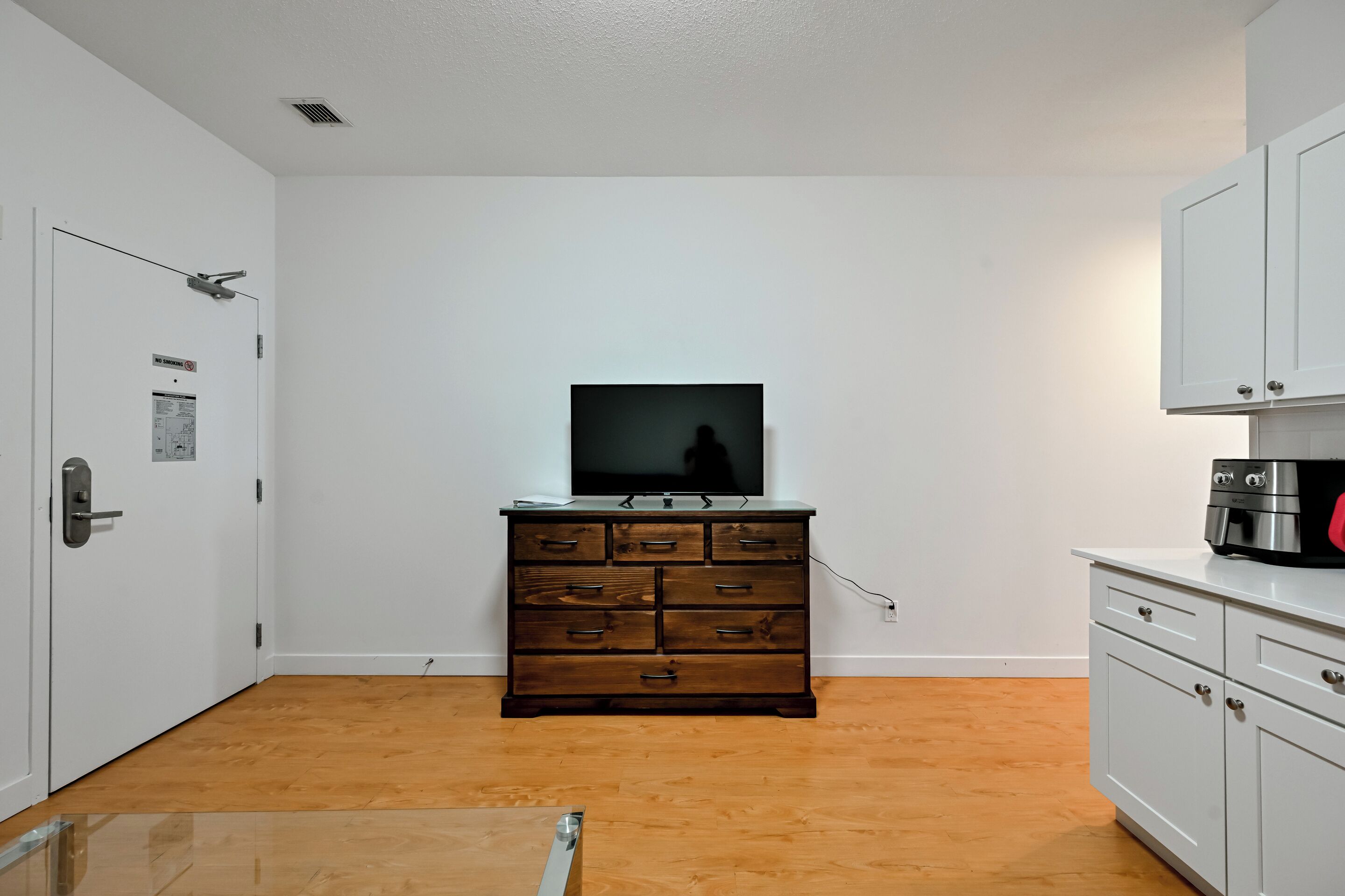 A room with a wooden dresser, a television on top, and a microwave on the right.