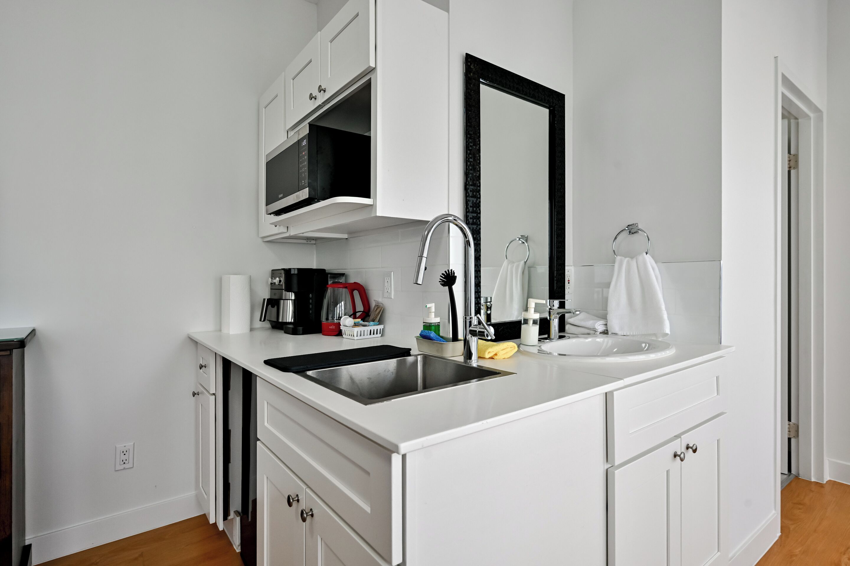 Una cucina moderna con mobili bianchi, un lavello doppio, un forno a microonde e un grande specchio sopra il lavello.