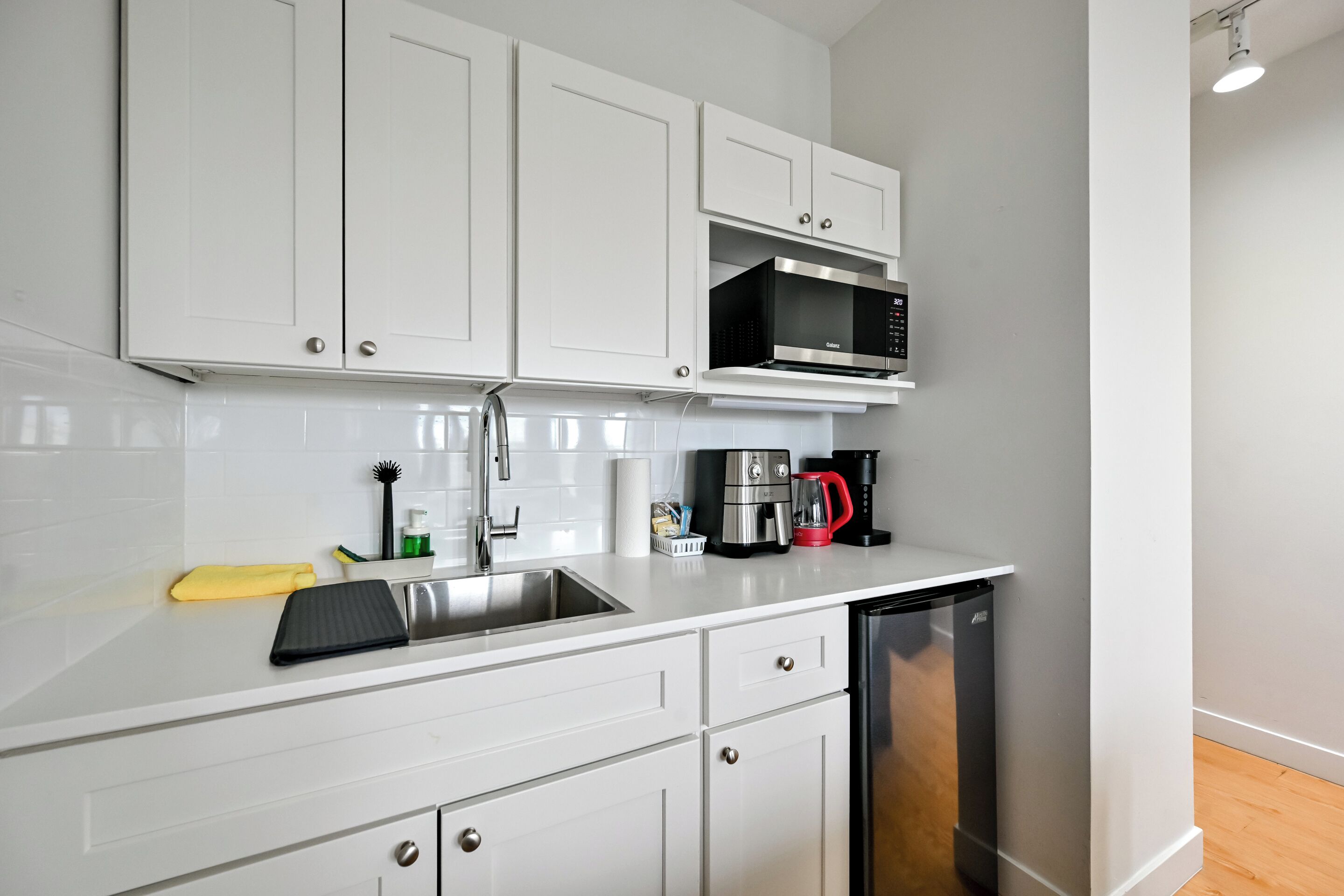 A modern kitchen with white cabinets, a stainless steel sink, a microwave, a coffee maker, and a dishwasher.