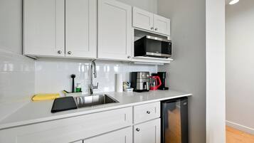 A modern kitchen with white cabinets, a stainless steel sink, a microwave, a coffee maker, and a dishwasher.