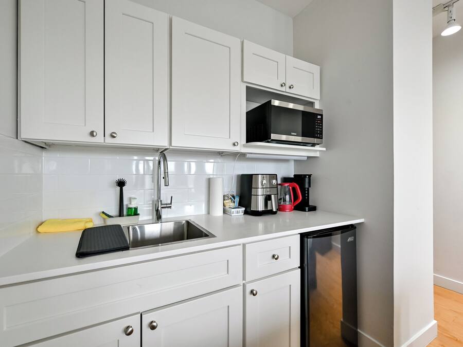 A modern kitchen with white cabinets, a stainless steel sink, a microwave, a coffee maker, and a dishwasher.