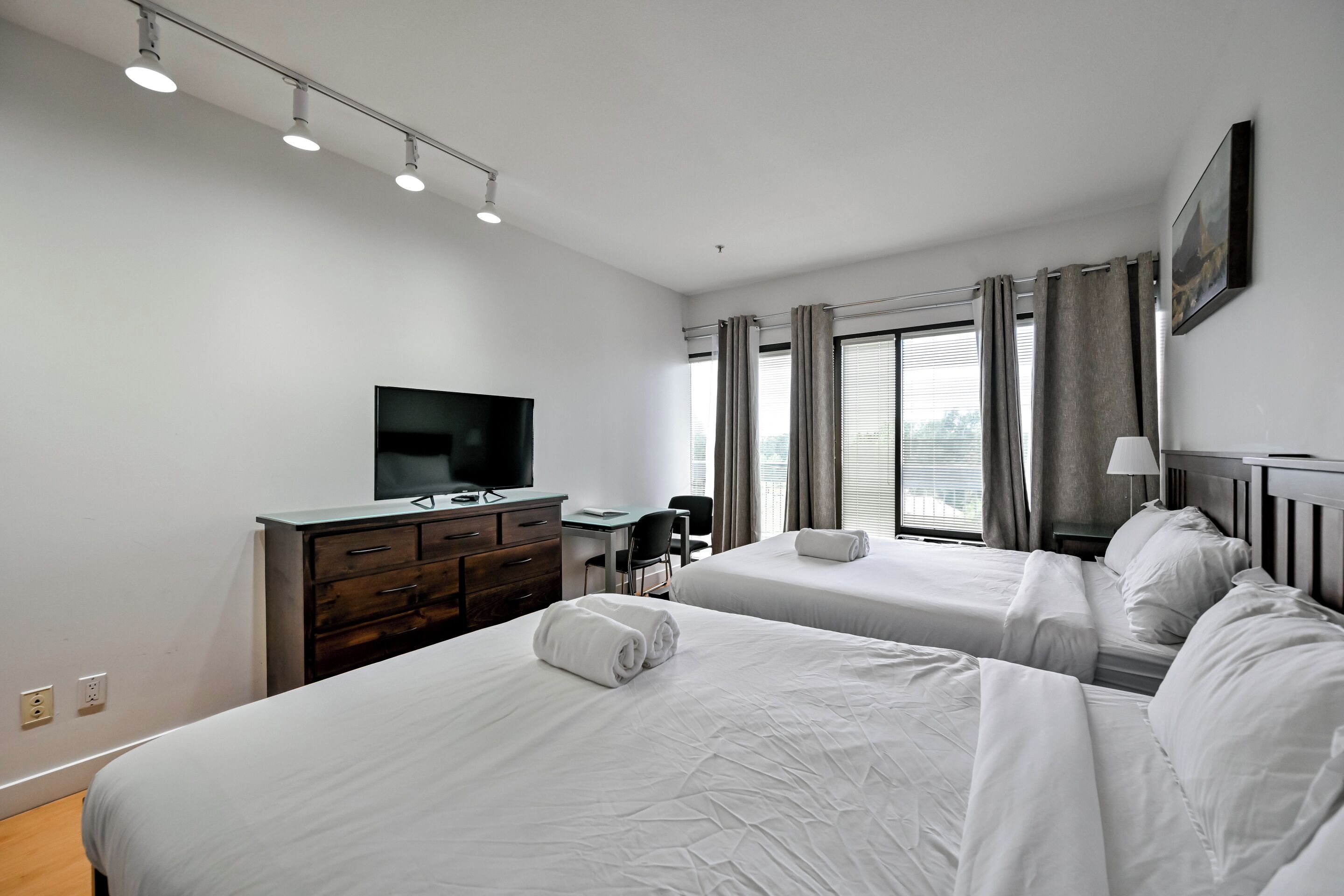 Quarto de hotel com duas camas, uma escrivaninha, televisão e janela com cortinas.