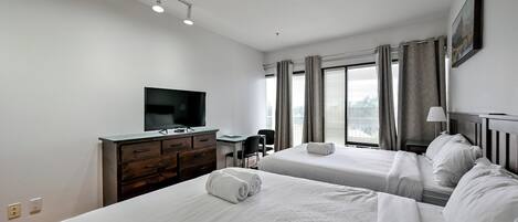 Habitación de hotel con dos camas, un escritorio, un televisor y una ventana con cortinas.