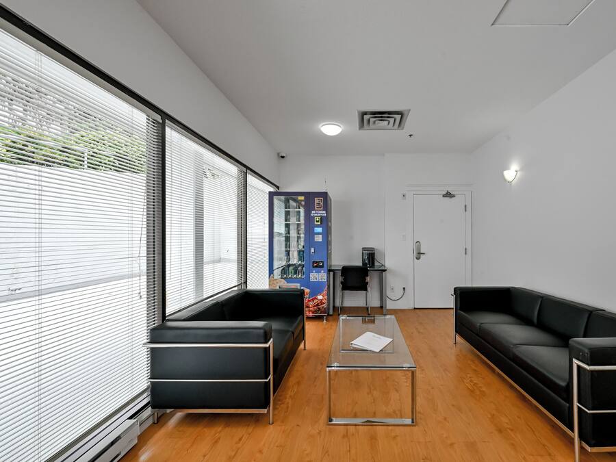 Un área de espera moderna con sofás de cuero negro, una mesa de centro de vidrio y una máquina expendedora.