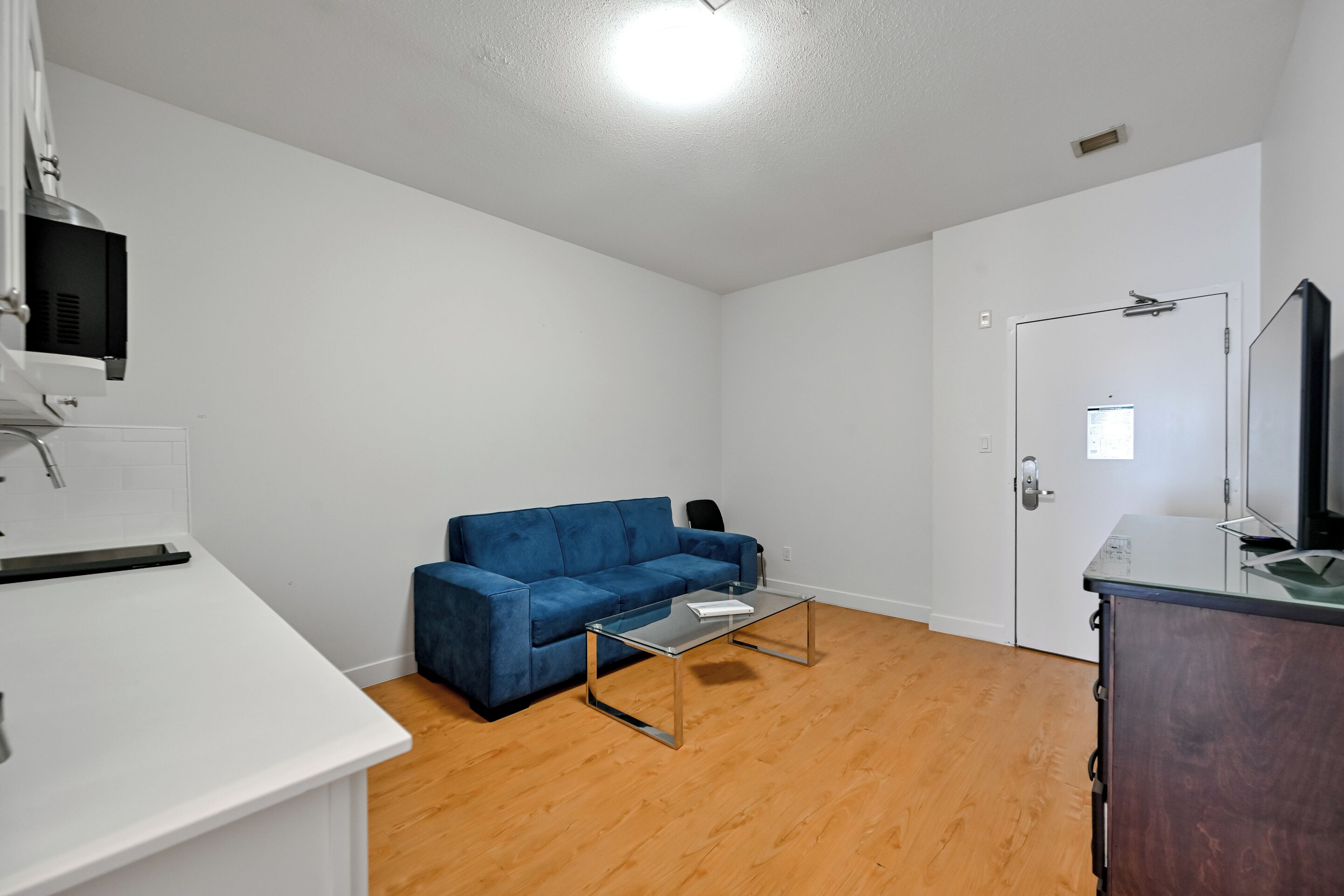 A room with a blue sofa, a glass coffee table, a white desk, and a wooden floor.