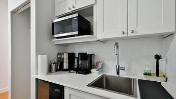 A modern kitchen with white cabinets, a stainless steel sink, a microwave, a coffee maker, and a dish rack.