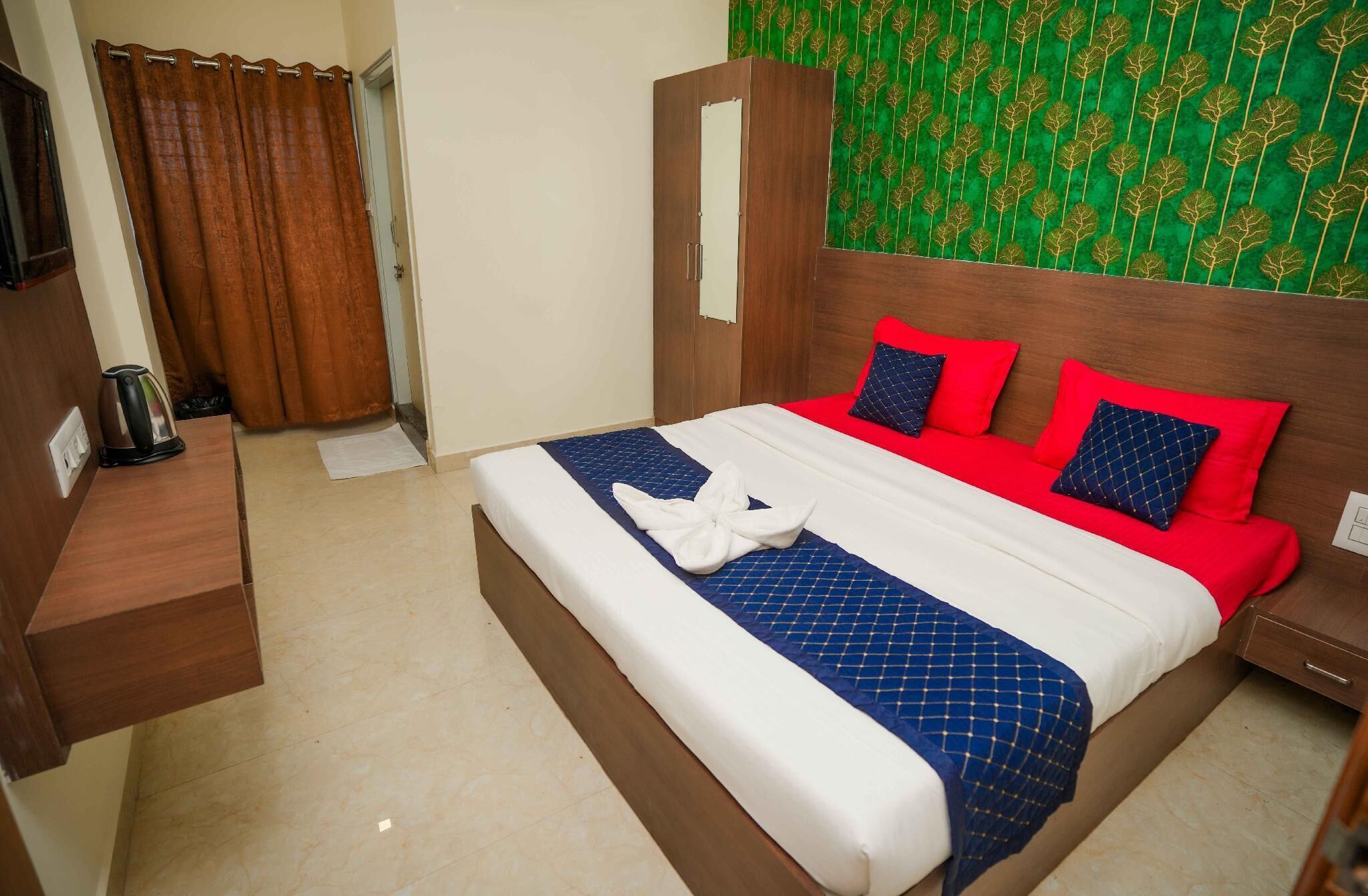 A hotel room with a bed, a wooden nightstand, a kettle, and a green patterned wall.