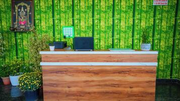 Una mesa de recepción con una computadora, un cuadro enmarcado y un letrero que indica los horarios de registro de entrada y salida.