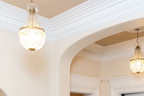 A room with two chandeliers, white walls, and a decorative ceiling.