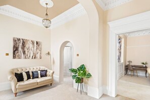 A spacious room with a cream-colored sofa, a large plant, and a desk with a chair.