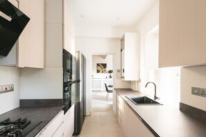 A modern kitchen with a gas stove, black refrigerator, and a sink. - Sneyd Park escape | Garden views by MyCityHaven (Sneyd Park)