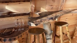 Un intérieur rustique en bois, avec des étagères où sont posés des mugs et un coin bar rustique agrémenté de tabourets.