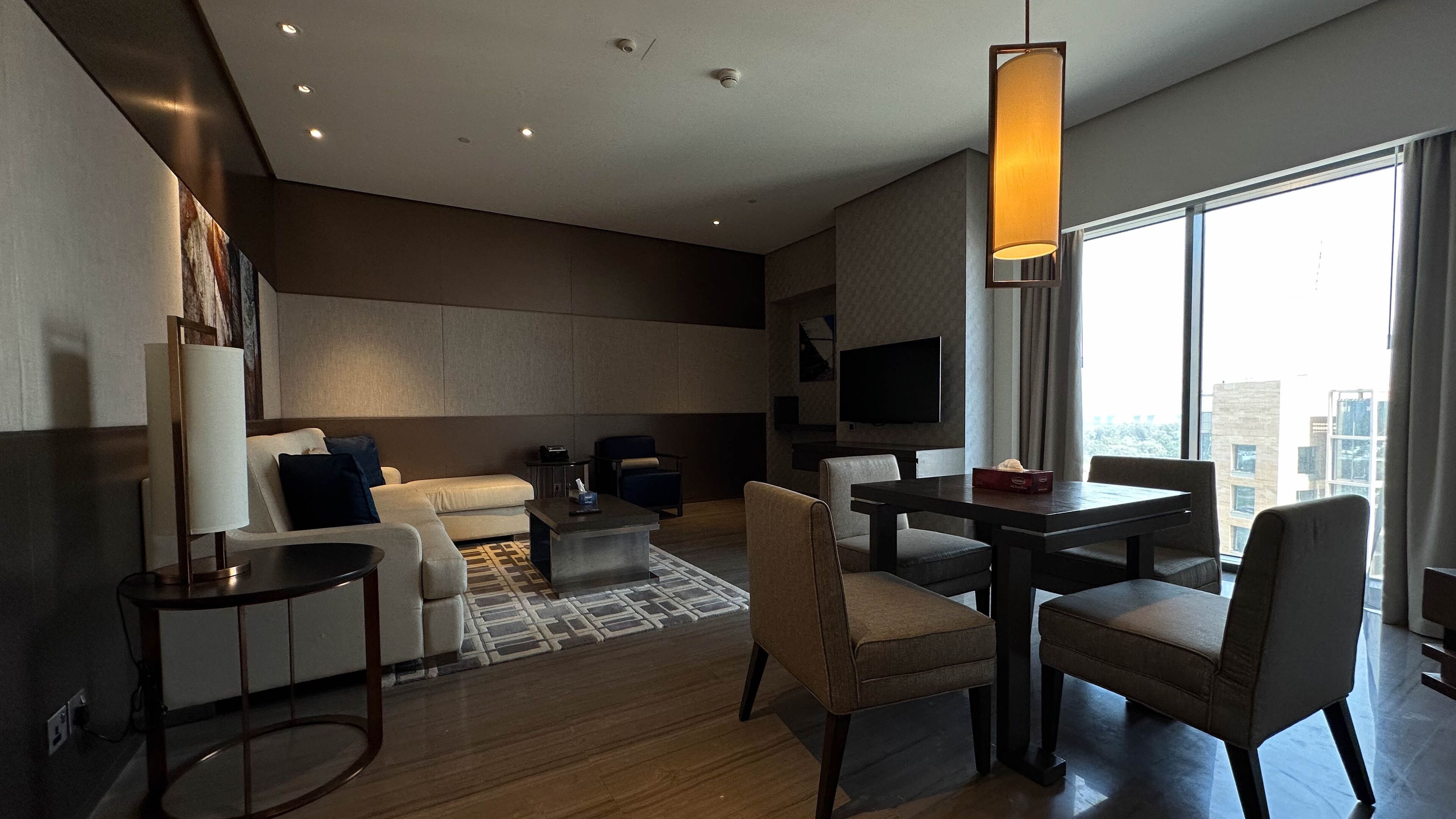 Een moderne hotelkamer met een bank, stoelen, een eettafel en een televisie.