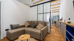 Ein zeitgemäßer Wohnbereich mit Ecksofa, Couchtisch aus Holz und einer Küche mit blauen Schränken.