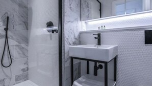 A modern bathroom with a glass-enclosed shower, a white sink with a black faucet, and a marble-tiled wall.