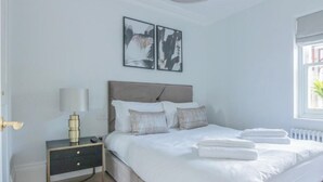 A bedroom with a bed, bedside tables, a lamp, and two wall-mounted pictures.