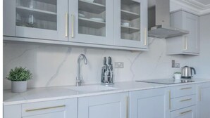 A modern kitchen with white cabinets, a stainless steel sink, and a marble backsplash.