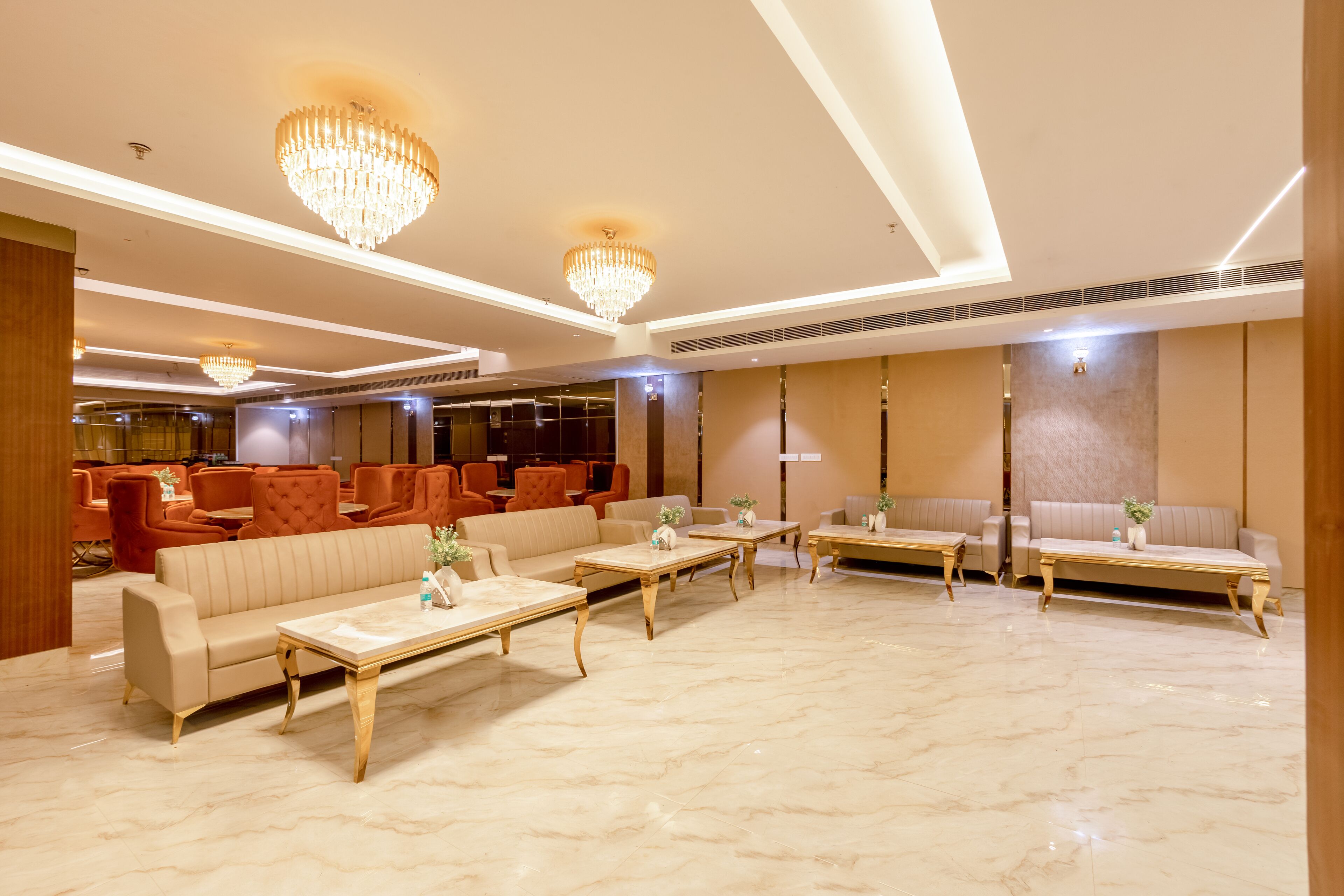A spacious lobby with a marble floor, multiple seating areas including sofas and armchairs, and large chandeliers.
