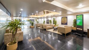 Un hall d’entrée moderne avec un sol noir poli, des canapés de couleur beige et des plantes en pot.