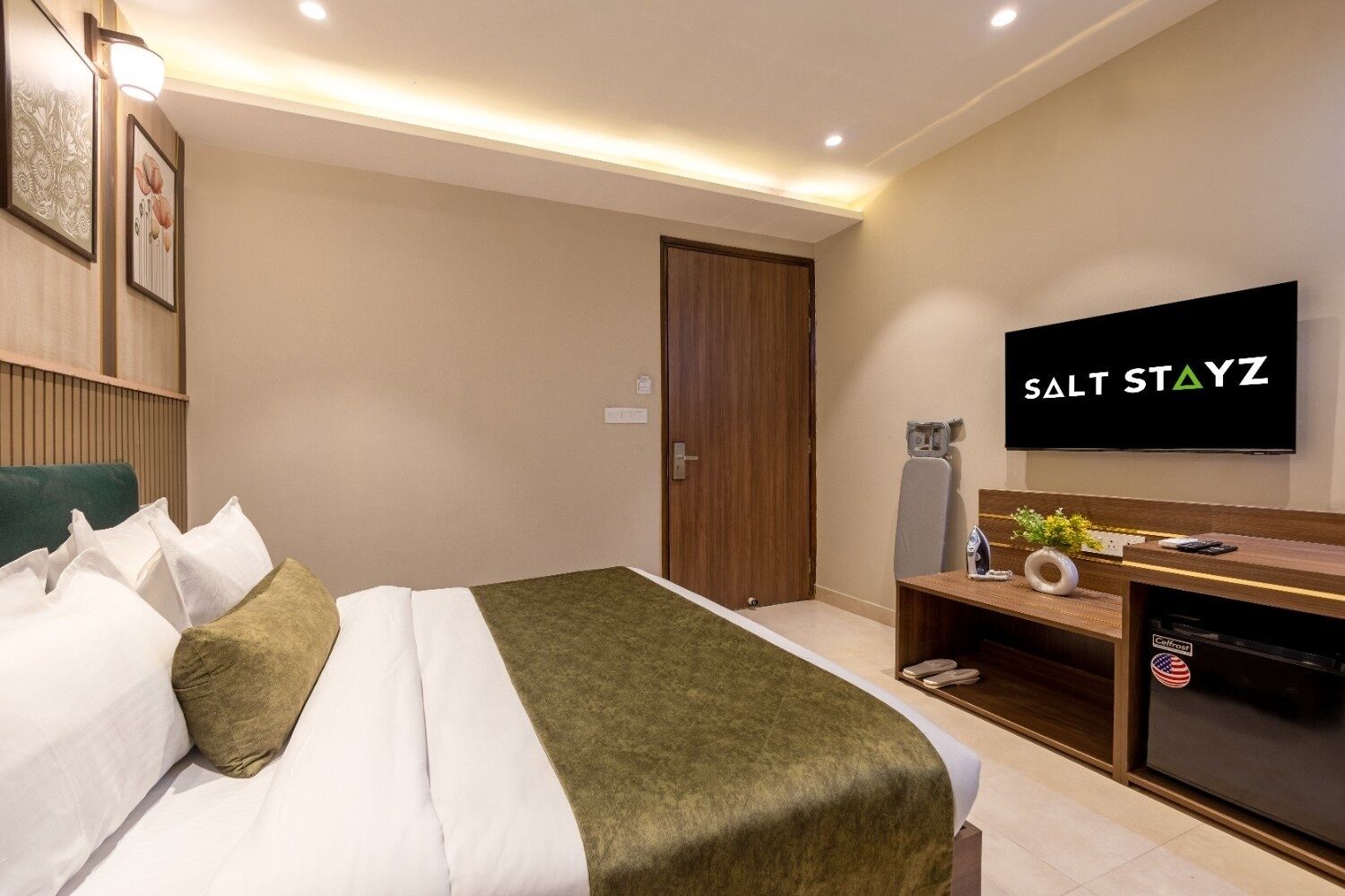 A hotel room with a bed, a television, a desk with a computer, and a door.