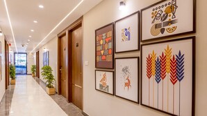 Un couloir orné de tableaux encadrés, équipé d’une caméra de surveillance et agrémenté de plantes en pot.