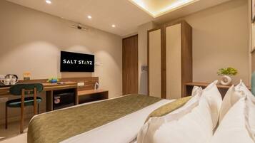 Quarto de hotel moderno com cama, escrivaninha, cadeira, televisão e guarda-roupa.