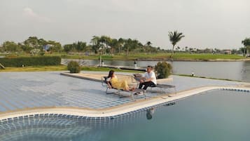 Relax by the pool surrounded by lush greenery and a serene body of water.