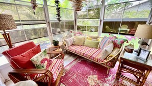 Una habitación acogedora y bien iluminada, con muebles de mimbre, un sofá estampado en rojo y blanco y una alfombra roja.