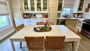 Una cocina moderna con armarios blancos, una mesa de comedor, sillas de mimbre y una bandeja decorativa.