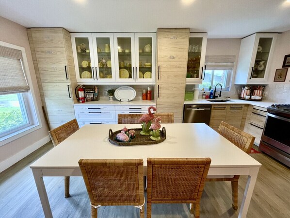 A modern kitchen with white cabinets, a dining table, wicker chairs, and a decorative tray.