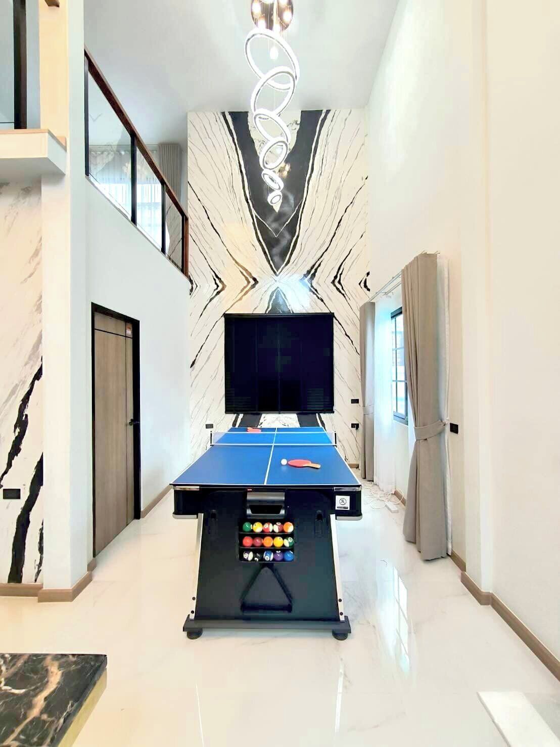 A spacious room with a pool table, a television, and a marble-patterned wall.