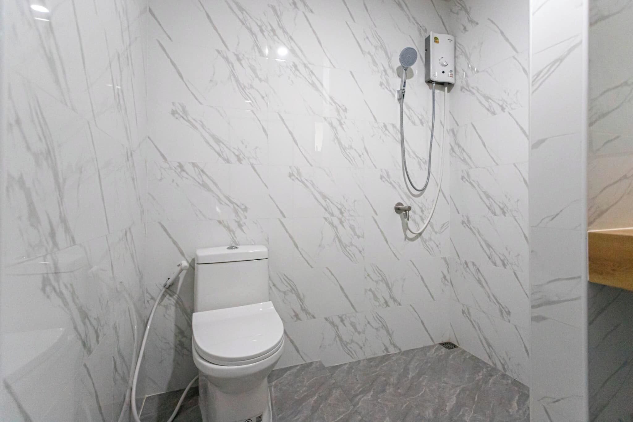 A bathroom with a toilet, a shower unit, and marble walls.