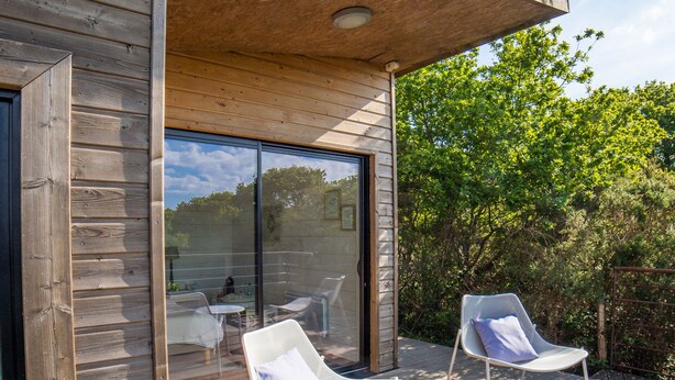 A wooden deck with two white lounge chairs and a small table, overlooking a garden.