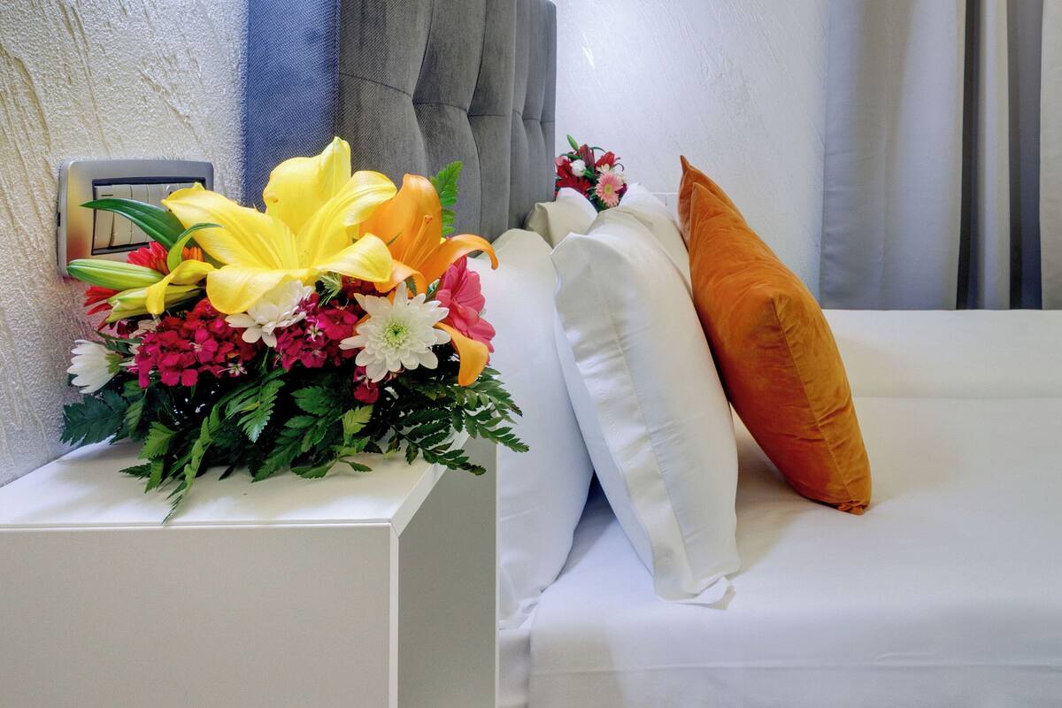 A hotel room with a neatly made bed, a bedside table with a floral arrangement, and a modern headboard.