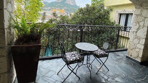 A stone balcony with a view of a mountain, a potted plant, and two chairs.
