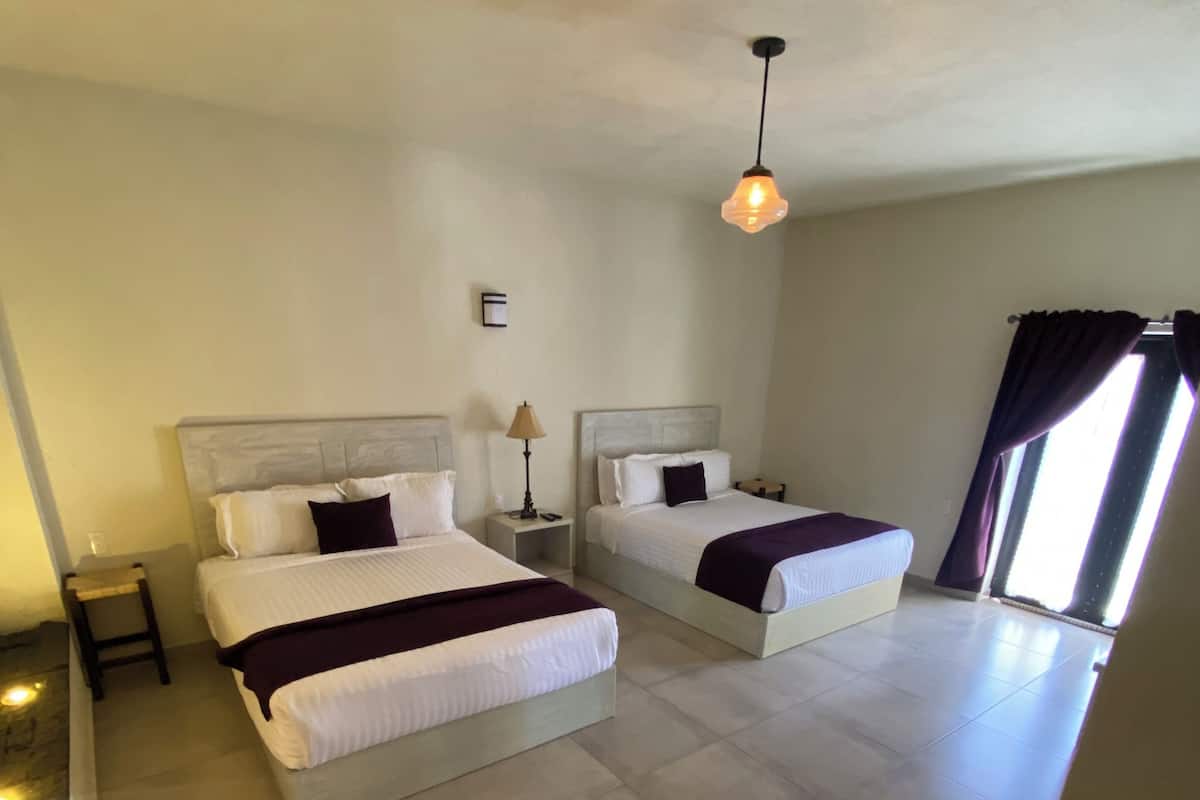 A hotel room with two beds, a nightstand, a lamp, and a ceiling light.