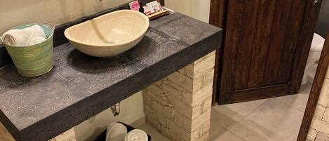 A bathroom with a stone sink, a green bucket, and a brown basket.