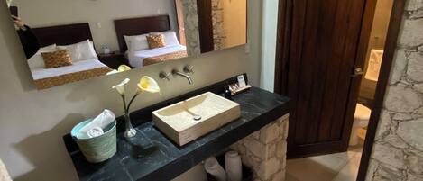 A bathroom with a stone archway, a large mirror, a wooden door, and a black countertop with a sink and towel storage.