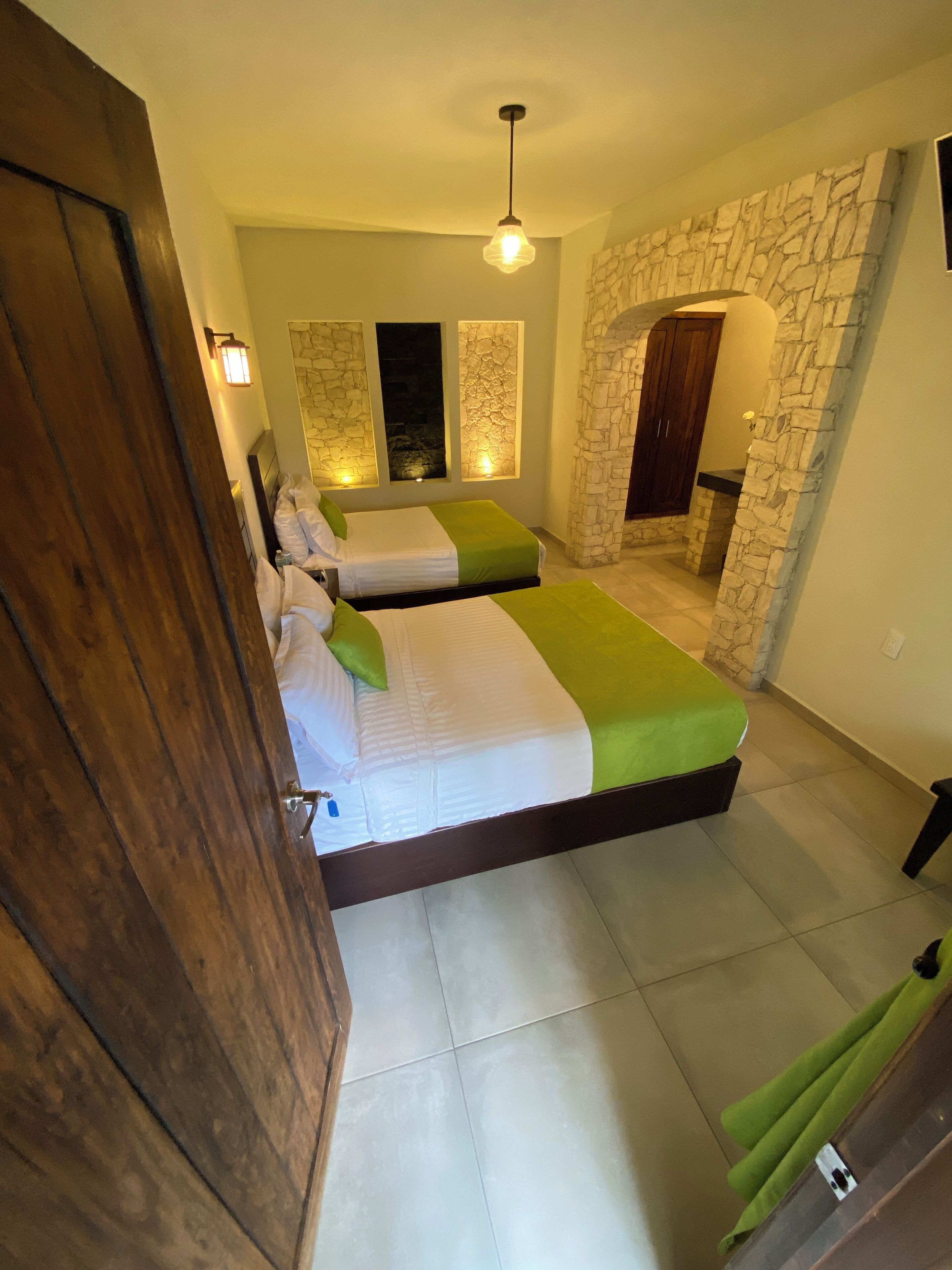 A hotel room with two beds, stone wall decor, and a wooden door.