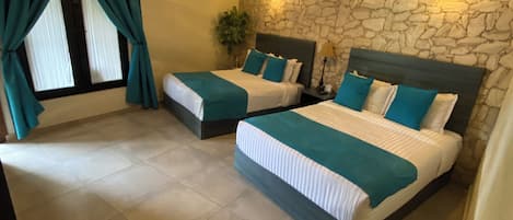 A room with two beds, a stone wall, a ceiling light, and a window with curtains.