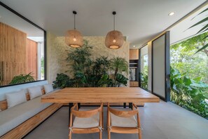 A modern dining area with a wooden table and chairs, a stone accent wall, and hanging wicker lamps. - The Luminous Villa Uluwatu  (Ungasan)