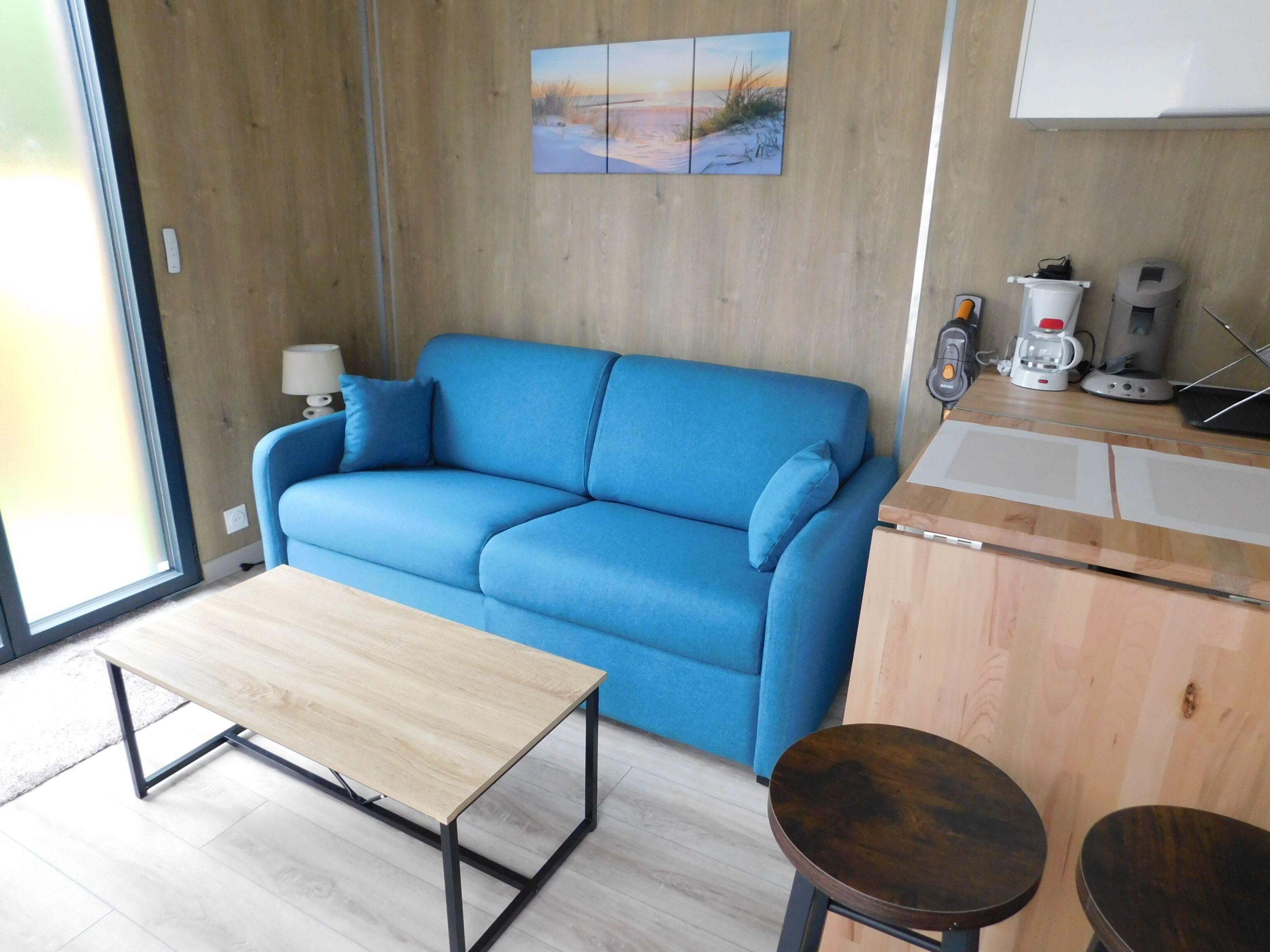 Un salon moderne avec un canapé bleu, une table basse en bois et un petit tabouret en bois.