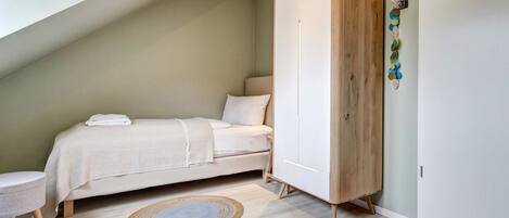 A bedroom with a bed, a wooden wardrobe, a round rug, and a small stool.